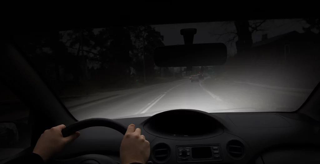 inside a car at night seeing the black road with headlights showing part of ahead